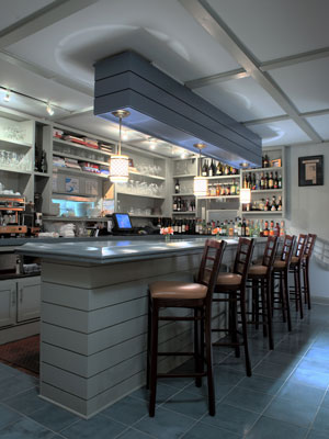 white and light blue bar counter and shelves lined with liquor bottles and glasses, and four chairs at bar