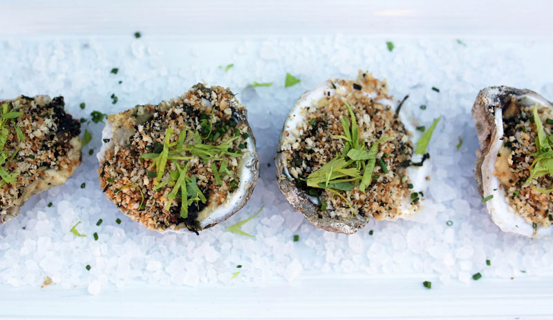 elegantly-plated close-up of four oysters rockefeller with bread crumbs