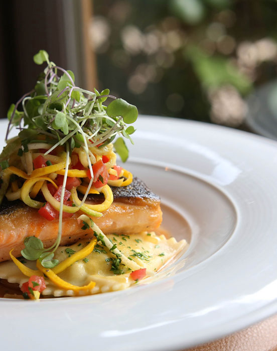 elegantly-plated dish of ravioli, salmon, top with chopped vegetables and sprouts